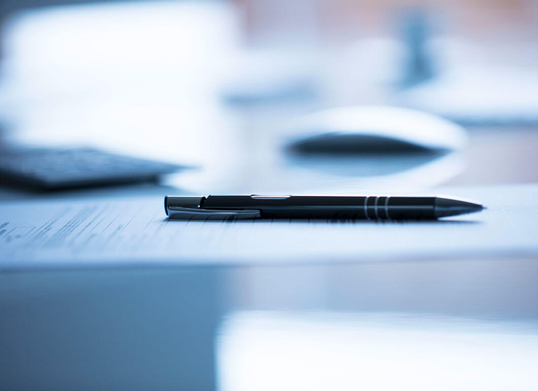 Black pen resting on paperwork on a shiny table.