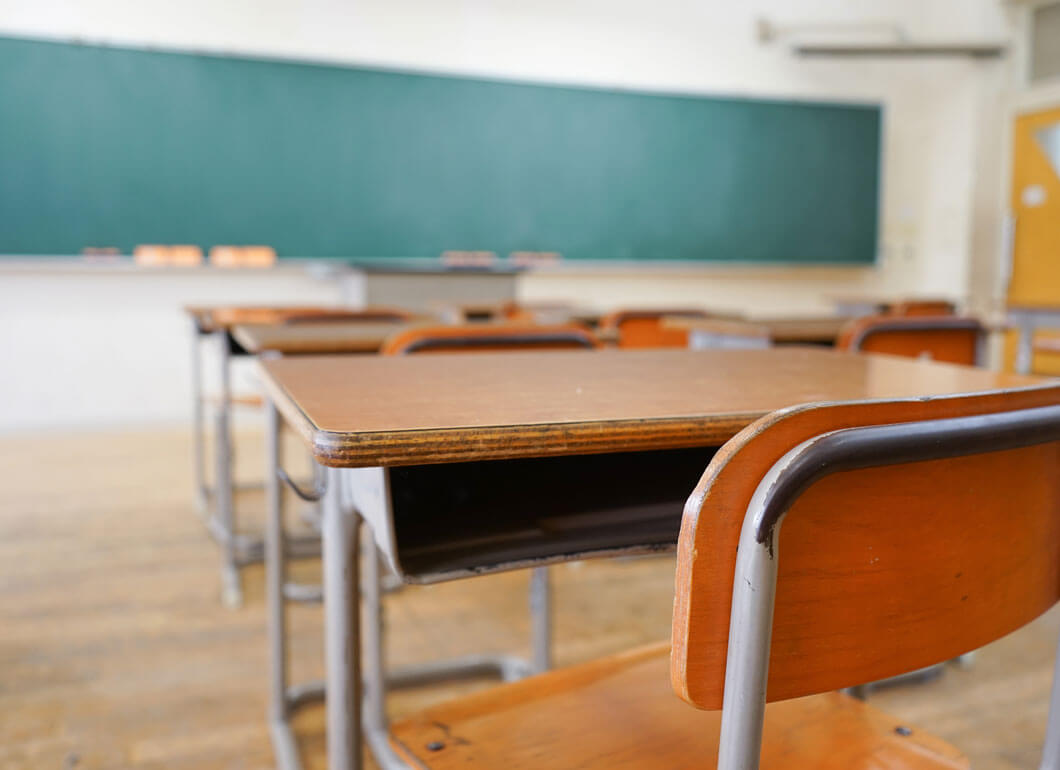 Old fashioned school desks pointing at a green chalkboard.