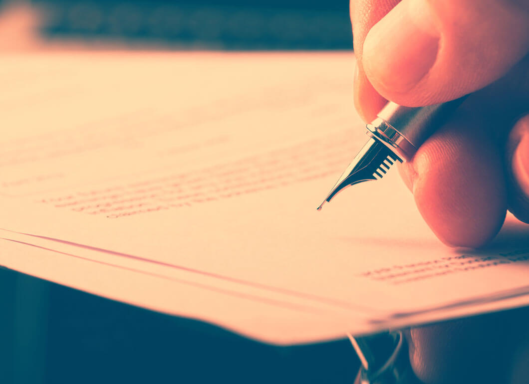 A person holding a pen and preparing to sign some paperwork.